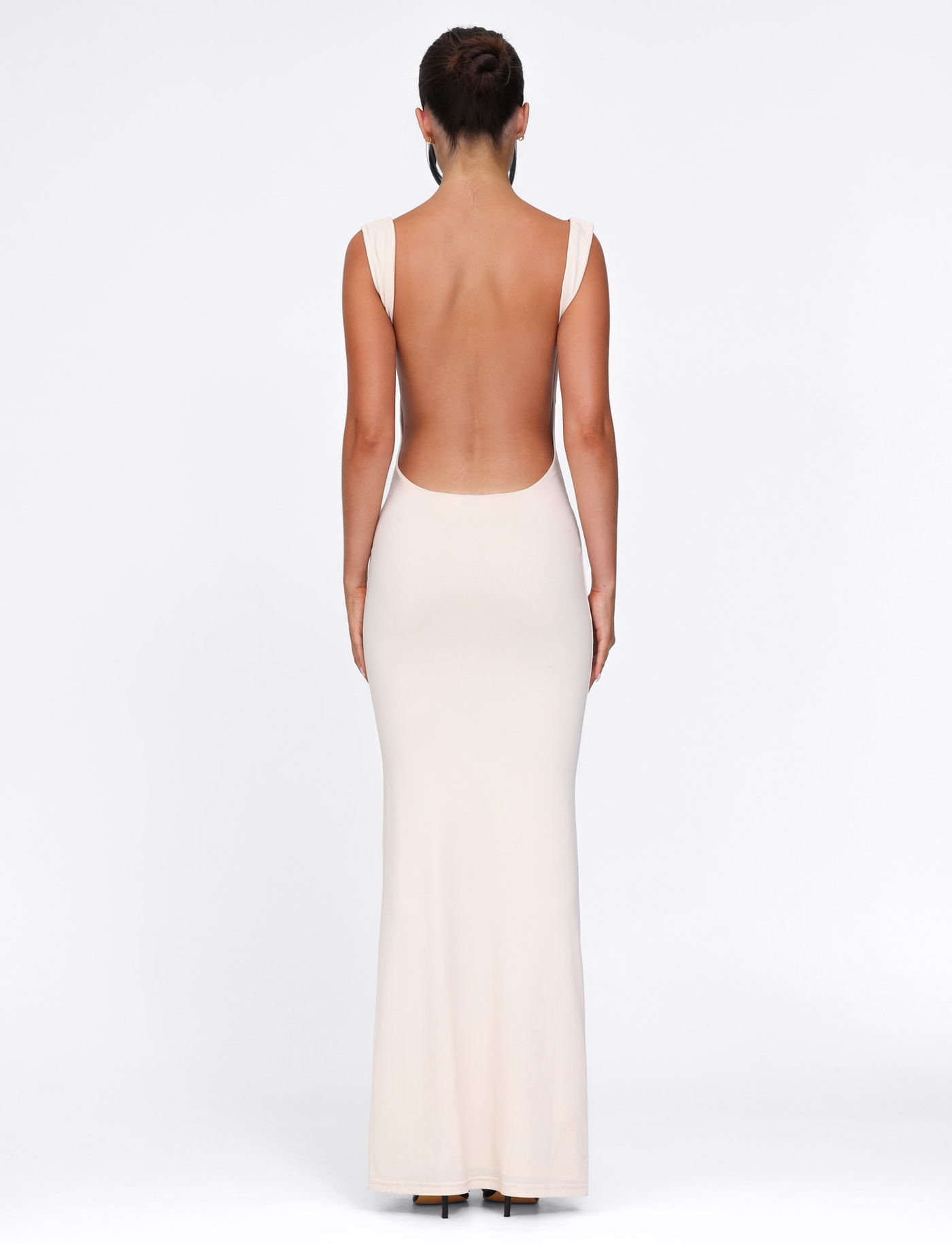 A woman with her hair in an updo poses against a white background, wearing the TIGERMIST MORANA DRESS - YELLOW : BUTTER—a long, sleeveless, backless bodycon dress. She is facing away from the camera.
