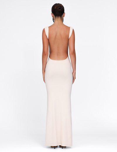 A woman with her hair in an updo poses against a white background, wearing the TIGERMIST MORANA DRESS - YELLOW : BUTTER—a long, sleeveless, backless bodycon dress. She is facing away from the camera.