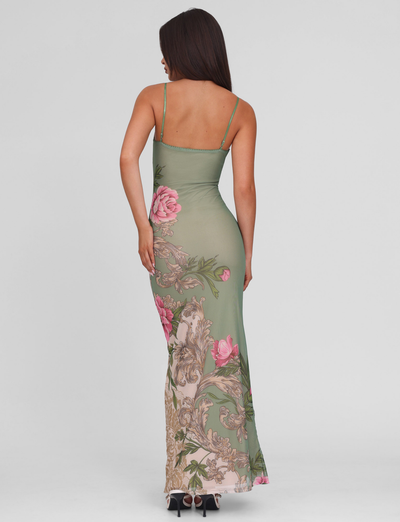 A woman stands with her back turned, wearing the TIGERMIST JULIANNA DRESS in green rococo floral and black high heels, against a plain light background.