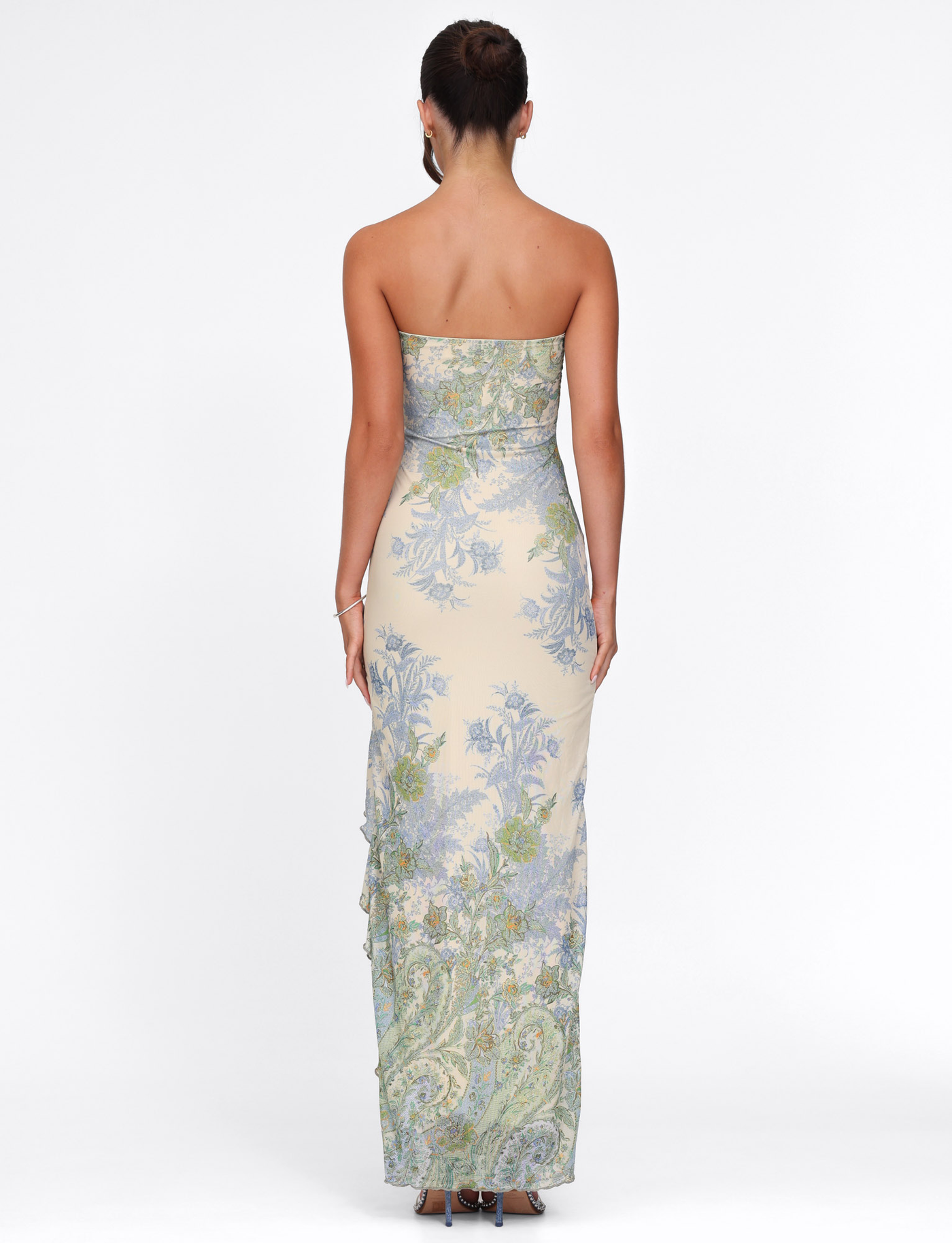A woman with her hair in a neat bun faces away, wearing the TIGERMIST THEO MAXI DRESS in Multi Paisley Tapestry print against a white backdrop.