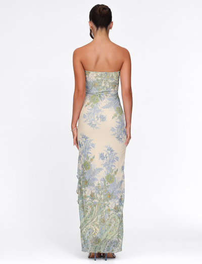 A woman with her hair in a neat bun faces away, wearing the TIGERMIST THEO MAXI DRESS in Multi Paisley Tapestry print against a white backdrop.