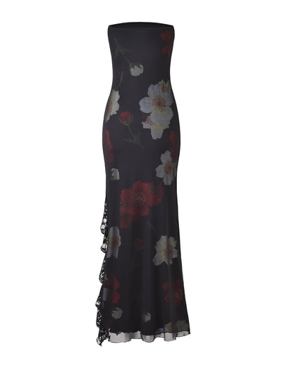 The Theo Maxi Dress - Red: Macro Floral by TIGERMIST is a strapless, floor-length black dress with a fitted silhouette. It features a striking red and white floral print and has a slight asymmetrical ruffle detail cascading down one side, adding an elegant touch.