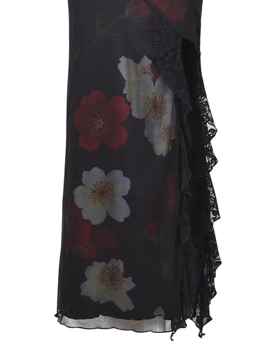 A close-up of the Theo Maxi Dress - Red: Macro Floral from TIGERMIST, showcasing its black fabric adorned with red and white floral designs. The dress is highlighted by a lace trim on the right side, complemented by cascading ruffles.